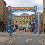 huddersfield, yest yorkshire, United Kingdom - 20 May 2019: the metal outdoor gate of huddersfield open market area and building in byram street with shops stalls and pedestrians